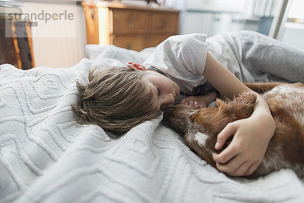 Süßer Junge kuschelnder Hund auf dem Bett