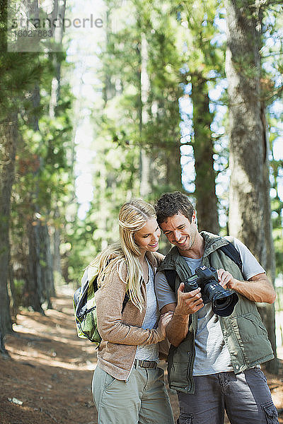 Lächelndes Paar schaut auf Digitalkamera im Wald