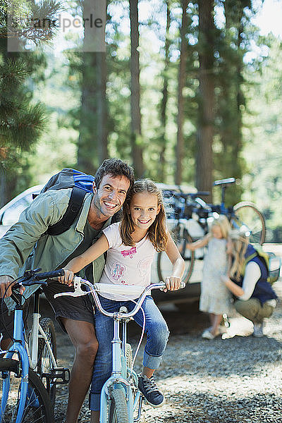 Lächelnder Vater und Tochter auf Fahrrädern im Wald
