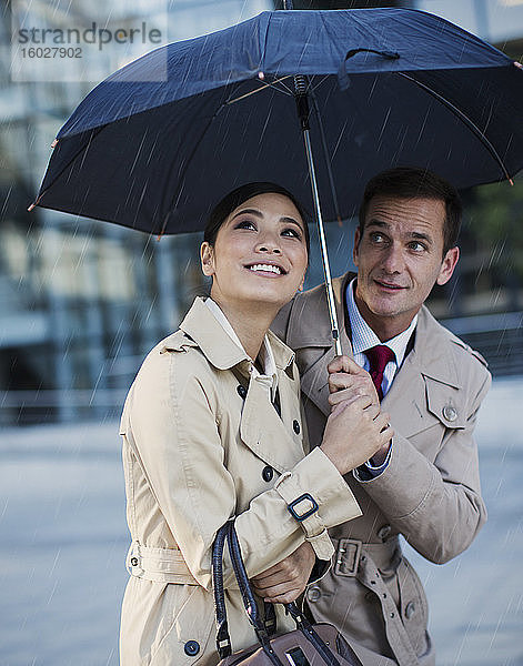 Geschäftsmann und Geschäftsfrau beobachten Regen unter einem Regenschirm
