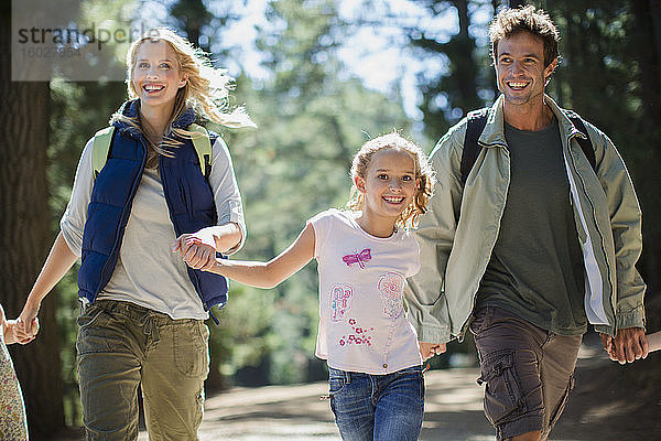 Lächelnde Familie hält Händchen und rennt im Wald