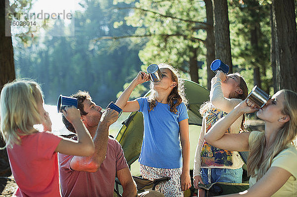 Familie trinkt aus Bechern auf einem Campingplatz im Wald