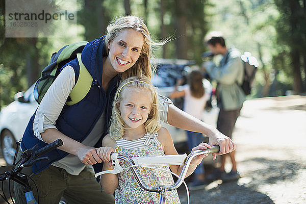 Lächelnde Mutter und Tochter mit Fahrrad im Wald