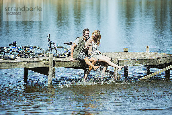 Paar auf dem Dock spritzt mit den Füßen im See