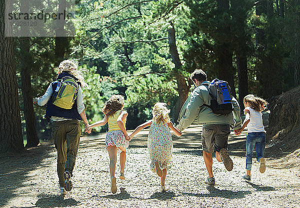 Familie hält Händchen und rennt im Wald