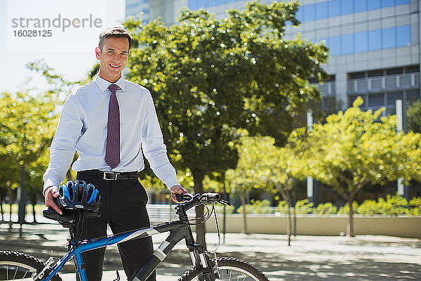 Lächelnder Geschäftsmann mit Fahrrad und Helm im Stadtpark