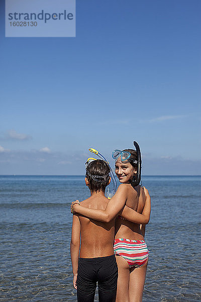 Bruder und Schwester tragen Schnorchel und umarmen sich am Strand