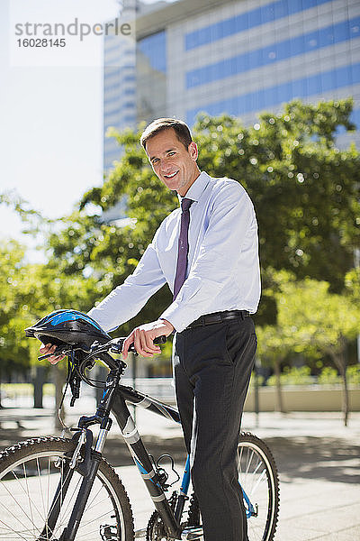 Lächelnder Geschäftsmann mit Fahrrad und Helm im Stadtpark