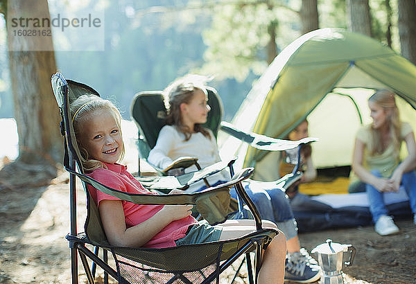 Lächelndes Mädchen sitzt auf einem Stuhl auf einem Campingplatz