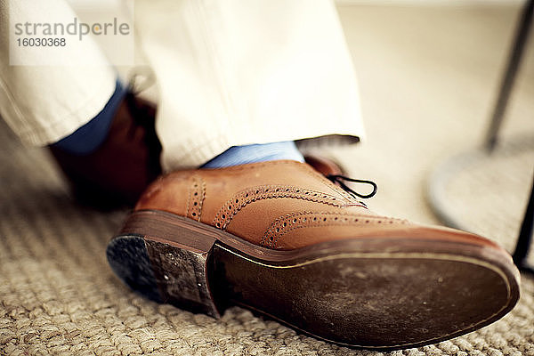 Nahaufnahme der Füße der Person  die braune Lederschuhe  blaue Socken und weiße Hosen trägt.