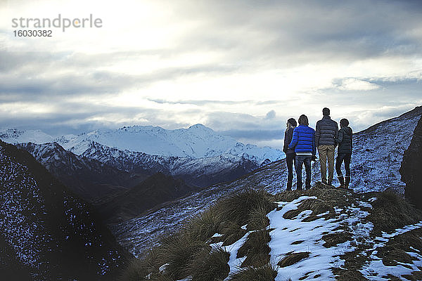 Rückansicht von vier nebeneinander stehenden Personen auf einem Berg  in der Ferne schneebedeckte Gipfel.