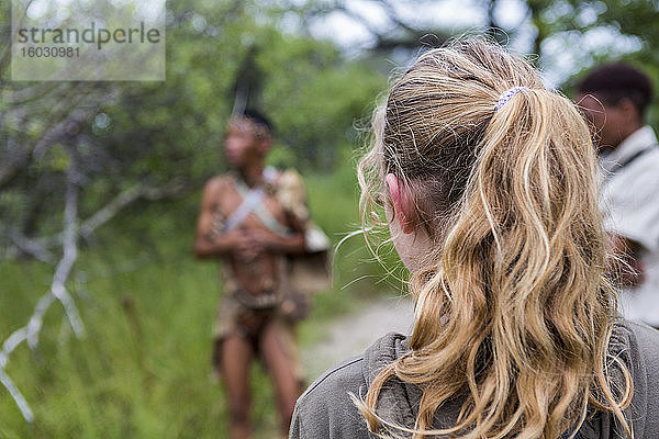 Rückansicht eines jugendlichen Mädchens  das mit einer Gruppe von Buschmännern aus dem Volk der San unterwegs ist.
