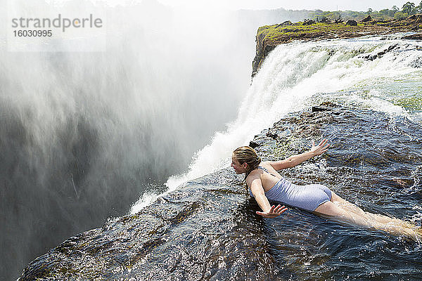 Junges Mädchen im Wasser am Devils Pool auf dem Bauch liegend  die Arme ausgebreitet  am Rande der Klippe der Victoriafälle.