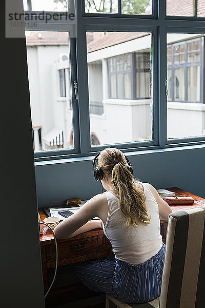 Ein dreizehnjähriges Mädchen mit Kopfhörern  das Hausaufgaben macht  sitzt an einem ruhigen Ort.