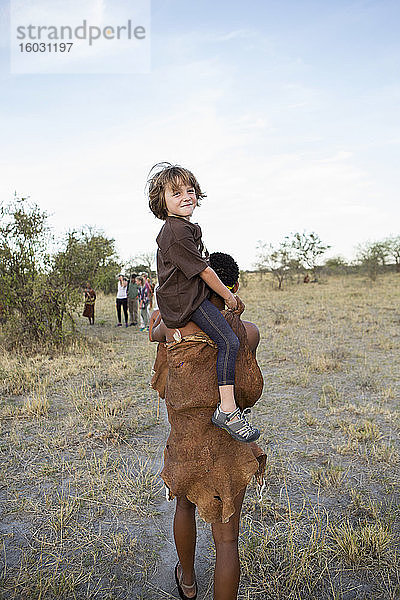 Fünfjähriger Junge  der auf den Schultern eines San-Buschmanns reitet.
