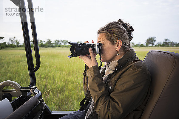 Erwachsene Frau mit Kamera sitzend in einem Safari-Jeep in offener Landschaft