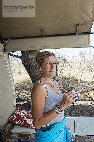 Eine erwachsene Frau mit einem Fernglas an einem Zelt in einem Wildreservat-Camp