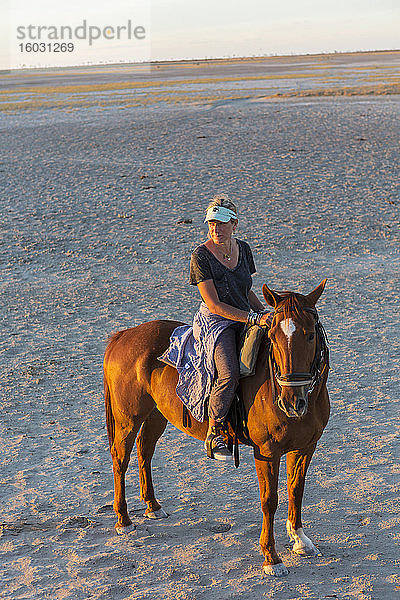 Eine Frau zu Pferd bei Sonnenuntergang im offenen Raum.