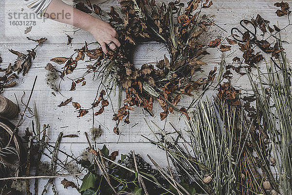 Frau fertigt einen kleinen Winterkranz aus getrockneten Pflanzen  braunen Blättern und Zweigen und Samenköpfen an.