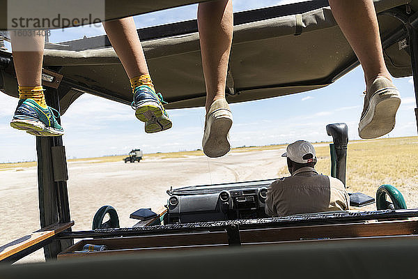 Ein Safari-Fahrzeug  eine Person auf dem Fahrersitz und zwei Sätze baumelnder Beine der Passagiere auf der Beobachtungsplattform.
