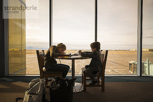 Ein Junge und seine ältere Schwester saßen an einem Tisch in einer Flughafenlounge und schrieben und zeichneten.