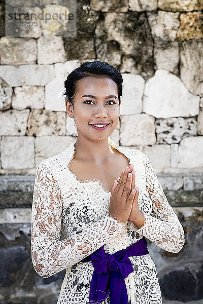 Eine junge balinesische Frau in einem lokalen Tempelkleid  die einen förmlichen Gruß macht und lächelt  Bali  Indonesien  Südostasien  Asien