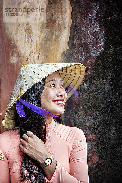 Eine junge Vietnamesin in traditionellem Ao-Dai-Kleid und Kegelhut und lächelnd  Farbton  Vietnam  Indochina  Südostasien  Asien