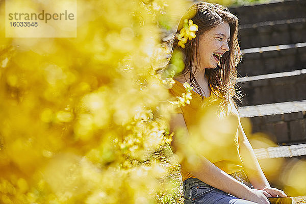 Teenagermädchen  das draußen auf Stufen sitzt  gelbe Forsythie im Vordergrund.