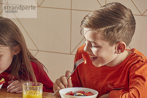 Junge und Mädchen sitzen am Küchentisch und essen Frühstück.