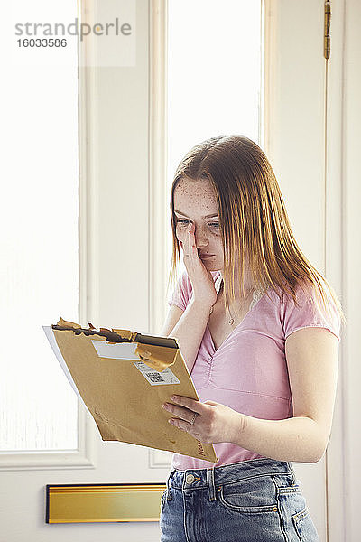 Ein junges Mädchen steht im Flur und hält einen großen Umschlag mit einem Brief in der Hand.