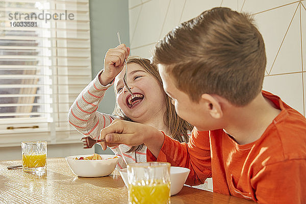 Junge und Mädchen sitzen am Küchentisch und essen Frühstück.