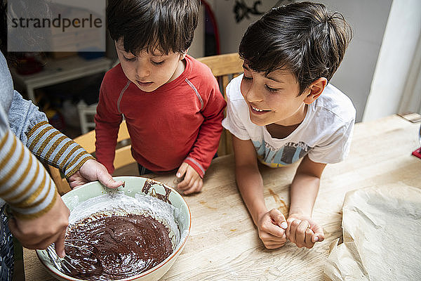 Zwei Jungen mit schwarzen Haaren sitzen an einem Küchentisch und backen Schokoladenkuchen.
