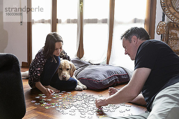 Vater und Tochter sitzen auf dem Boden des Wohnzimmers und puzzeln während der Coronavirus-Sperre.