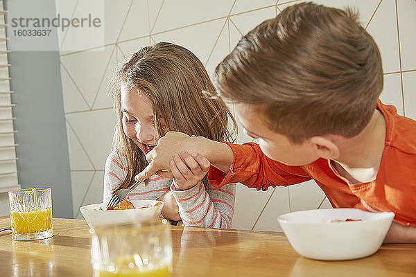 Junge und Mädchen sitzen am Küchentisch und essen Frühstück.