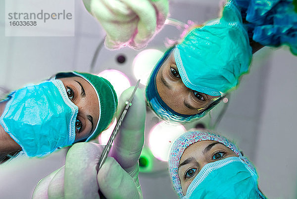 Niedrigwinkelansicht von drei Chirurginnen mit Operationsmasken  die in die Kamera schauen.