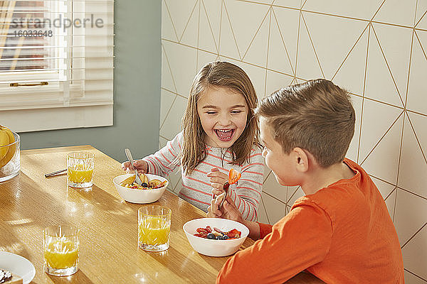 Junge und Mädchen sitzen am Küchentisch und essen Frühstück.