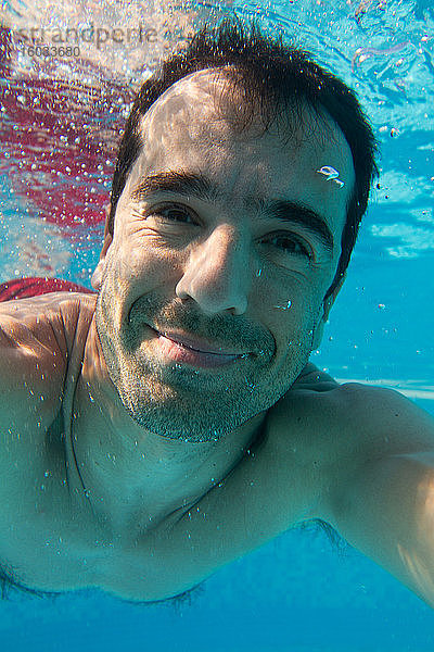 Ein Mann schwimmt unter Wasser  lächelt eine Kamera an  ein Unterwasser-Selfie.
