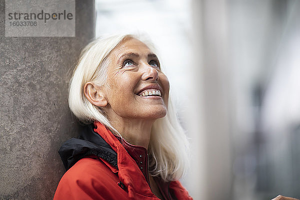Bildnis einer lächelnden Frau mit langen weißen Haaren  die im Freien steht und nach oben schaut.