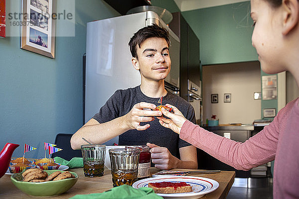 Junge und Mädchen sitzen am Küchentisch und essen Muffins.