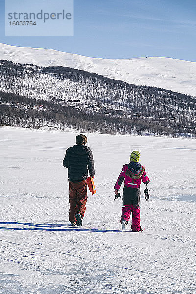 Rückansicht von zwei Jungen  die auf einem zugefrorenen See in Vasterbottens Lan  Schweden  spazieren gehen.