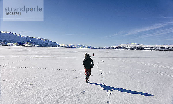 Rückansicht von zwei Jungen  die über den zugefrorenen See in Vasterbottens Lan  Schweden  laufen.