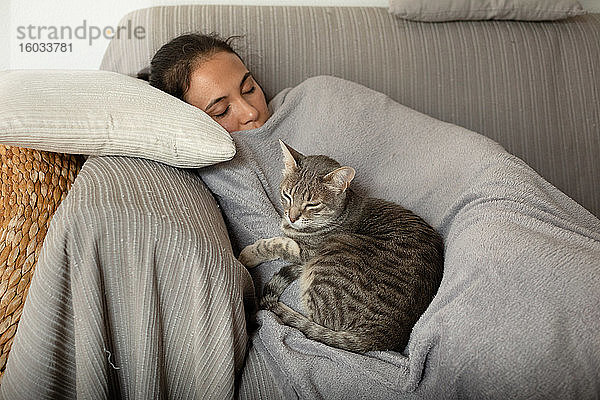 Frau und grau gestromte Katze schlafen auf einem Sofa.