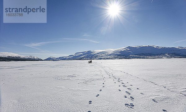 Blick über den gefrorenen See mit Menschen in der Ferne  drei Spuren von Fußabdrücken
