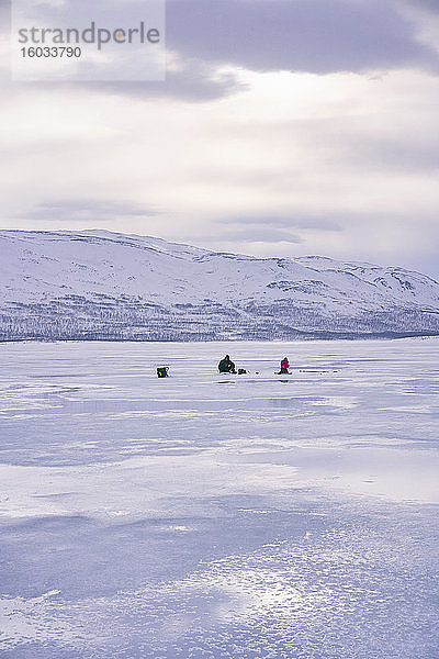 Fernblick von zwei Personen beim Eisfischen auf dem zugefrorenen See in Vasterbottens Lan  Schweden.