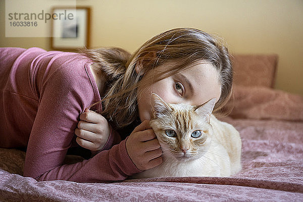 Porträt eines Mädchens und einer weißen und rothaarigen Katze auf dem Bett liegend.