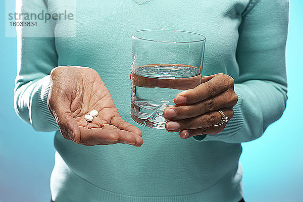 Nahaufnahme einer Frau  die Tabletten und ein Glas Wasser hält  auf blauem Hintergrund.