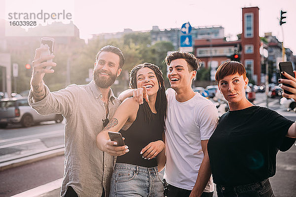 Zwei junge Frauen und Männer in legerer Kleidung auf einem Dach stehend  die sich mit einem Mobiltelefon selbstständig machen.