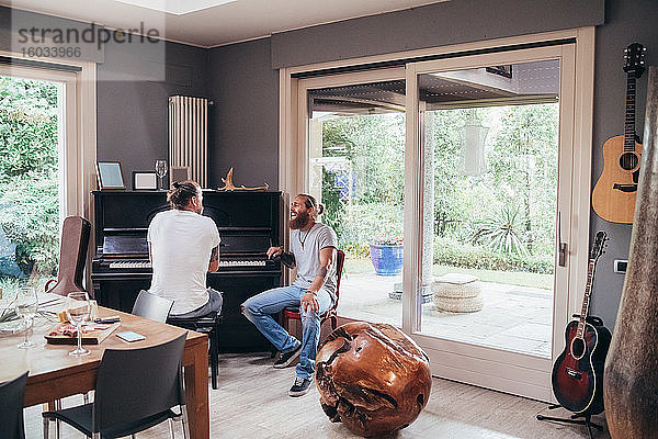 Zwei bärtige tätowierte Männer mit langen brünetten Haaren sitzen lachend an einem Klavier.