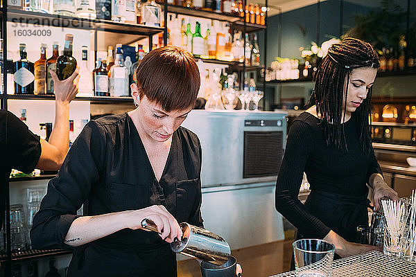 Zwei schwarz gekleidete junge Frauen stehen hinter der Theke und bereiten Getränke vor.