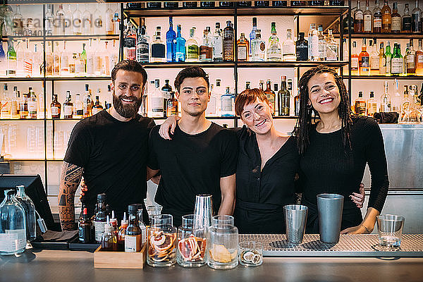 Porträt von zwei jungen Frauen und Männern in schwarzer Kleidung  die in einer Bar arbeiten und in die Kamera lächeln.